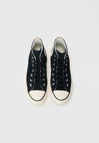 Μαύρα ψηλά αθλητικά παπούτσια από καμβά με λευκές λαστιχένιες μύτες, μαύρα κορδόνια και ασημένια οπές. Υφή σόλας και αντίθετη ραφή.