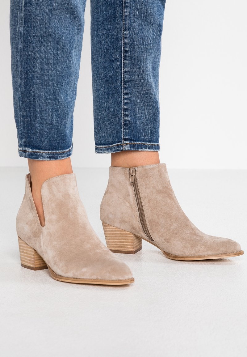 Bottines beiges en daim avec fermeture éclair latérale, talons en bois empilés, portées avec un jean denim bleu raccourci.