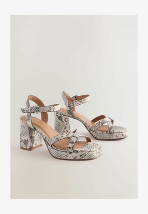 Pumped kurpes ar čūskādainu rakstu, ar krusteniskām siksnām, masīvām blokveida papēžiem un gludu bēša krāsas zoli.