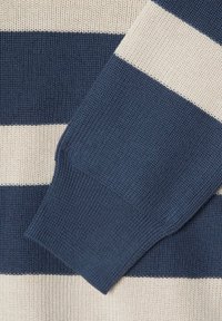 Pleteni pulover s mornarsko plavim i krem trakama. Tekstura je rebrasta, s dugim rukavima i uskim manžetama.