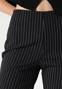 Pantalons à rayures noires en tissu, présentant des lignes verticales blanches étroites, coupe ajustée, texture lisse et détail à la taille.