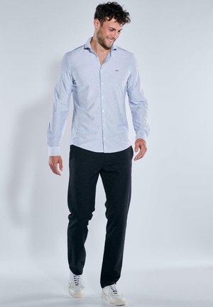 Hellblaues, gestreiftes Hemd zum Knöpfen mit langen Ärmeln, kombiniert mit dunkler Hose und weißen Turnschuhen. Das Hemd verfügt über ein dezentes Logo und einen klassischen Kragen.