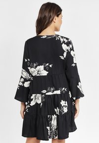 Schwarzes Kleid mit weißem Blumenmuster, ausgestelltem Ärmel, gestuftem Rüschensaum und glattem Stoff. Verfügt über eine lockere Passform und einen runden Ausschnitt.