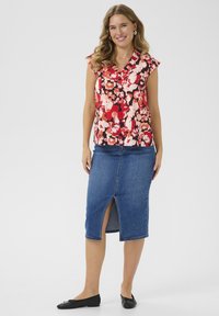 Haut à motif floral en rouge, rose et blanc, avec de courtes manches volantées. Jupe crayon en denim avec une fente à l'avant. Chaussures plates noires.
