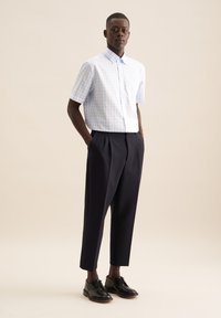 Camicia a maniche corte a quadri blu chiaro e bianco abbinata a pantaloni neri plissettati e scarpe nere lucide. Design semplice e strutturato.