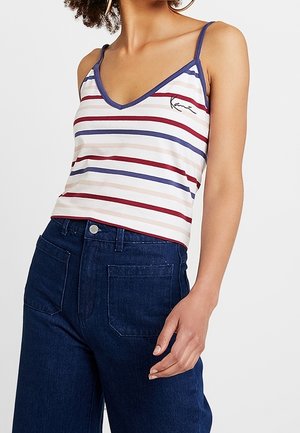 Kobieta ubrana w bezrękawnik w paski w kolorach granatowym, czerwonym i beżowym, zestawiony z ciemnoniebieskimi jeansami z wysokim stanem.