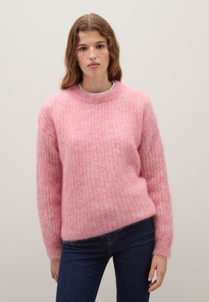 Rosa, flauschiger Pullover mit rundem Ausschnitt und gerippten Bündchen, in lockerer Passform und mit strukturiertem Oberflächenmaterial. Kombiniert mit dunkelblauen Jeans.