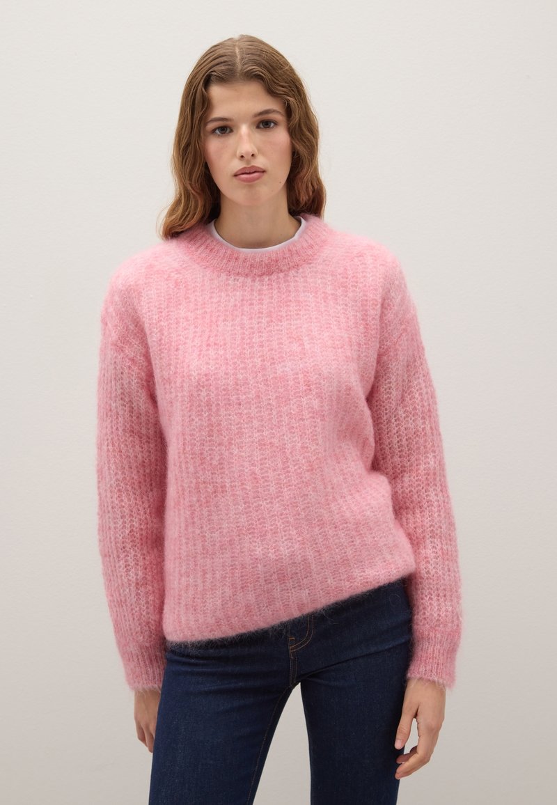 Maglione rosa e morbido con scollatura rotonda e polsini a costine, caratterizzato da una vestibilità ampia e una superficie testurizzata. Abbinato a jeans blu scuro.