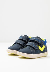 Modré a žluté suché zipy s gumovou podrážkou, s prošívanými detaily a logem na pásku. Akcentní barva v designu.