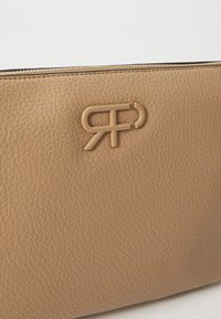 Beżowa skórzana torebka z teksturową powierzchnią i wyraźnym wytłoczonym logo. Główne zapięcie na zamek błyskawiczny z metalowymi akcentami.