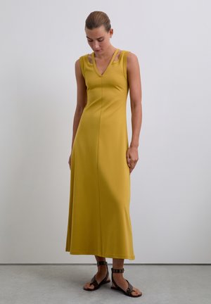 Abito midi giallo senza maniche con scollatura a V, dettagli in riga sulle spalle e una silhouette aderente, abbinato a sandali neri con cinturini.