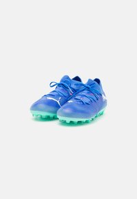 Botas de fútbol azules hechas de material sintético texturizado, con cierre de cordones, acentos de color azul claro y una suela transparente verde con tacos.