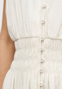 Vestido de tela blanca texturizada con botones verticales en la parte delantera y una sección de cintura elástica y fruncida.