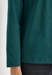 Teal langärmliges Shirt aus einem weichen, strukturierten Stoff, mit einem geraden Saum und einfachen Nähten an den Bündchen.