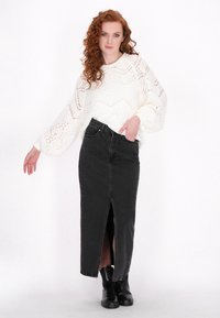 Biały sweter dziergany w geometryczny wzór, zestawiony z czarną spódnicą dżinsową z przednim rozcięciem, noszony z czarnymi botkami za kostkę.