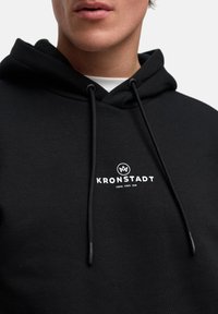 Svart hettegenser med snøring og logo samt tekst i hvitt. Laget av myk stoff, med ribbede mansjetter og hem. 