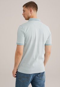 Polo de culoare bleu deschis cu textură în relief, guler în contrast și mâneci scurte. Purtați cu blugi, evidențiind un stil casual.