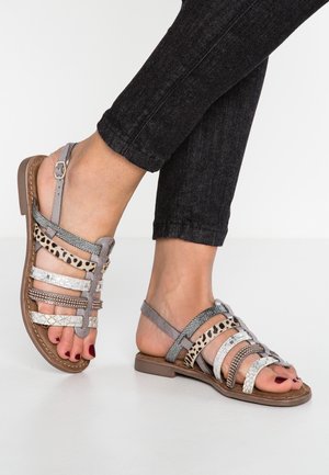Grijze sandalen met bandjes van gemengde materialen, waaronder dierenprint, metalen accenten en een platte bruine zool. Verstelbare enkelband.