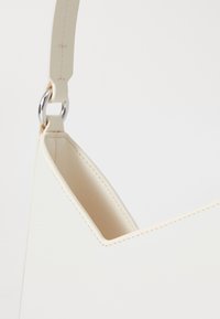 Borsa a spalla in pelle crema dal design elegante, con una parte superiore arrotondata, cuciture visibili e un accento in metallo argentato sulla tracolla.