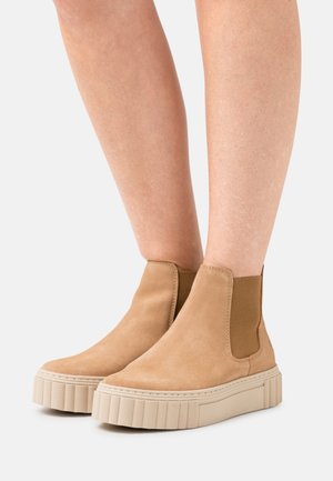 Bottes chelsea en suede beige avec panneaux élastiques sur les côtés et une semelle plateforme épaisse crème avec des rainures verticales.