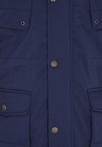 Chaqueta azul marino vista frontal con cuatro botones de presión plateados, dos bolsillos con solapa en la parte inferior y dos bolsillos más pequeños en el pecho con ojales metálicos.