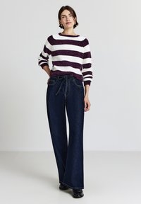 Striped sweater in white and dark purple knit, paired with wide-leg dark blue denim jeans featuring a belted waist and side pockets.