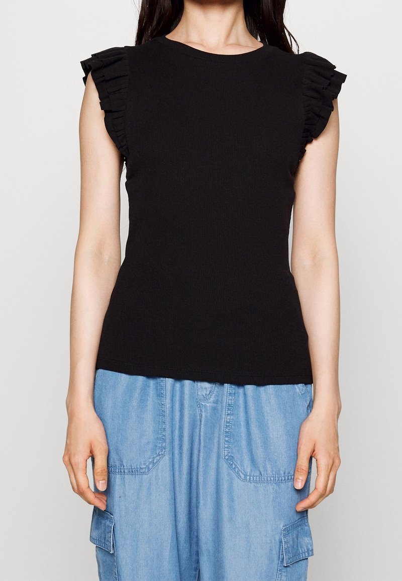 Top in tessuto a coste nera con spalline arricciate. Indossato con pantaloni cargo larghi di colore blu chiaro con tasche frontali.