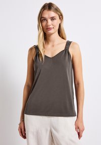 Top senza maniche grigio scuro con scollatura a V. Presenta spalline annodate e tessuto morbido e liscio, abbinato a pantaloni chiari e larghi.