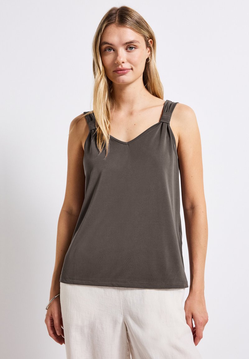Top senza maniche grigio scuro con scollatura a V. Presenta spalline annodate e tessuto morbido e liscio, abbinato a pantaloni chiari e larghi.