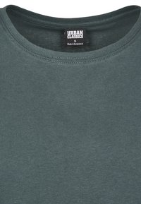 T-shirt en coton vert foncé avec un col arrondi. Présente un design simple et comprend une étiquette indiquant "URBAN CLASSICS" et la taille "S."