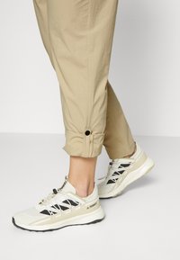 Vita och svarta träningsskor har en ovandel av nät och sula av gummi, designade för grepp. Matchas med ljusbeige uppvikta byxor.