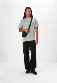 Gray short-sleeve t-shirt with purple graphic, paired with black wide-leg pants and black sneakers. Black crossbody bag worn on left.