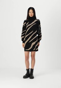 Strickkleid mit schwarzem Grund und beigen Zebra-Streifen, hohen Kragen und voluminösen Ärmeln. Kombiniert mit schwarzen Kampfboots und einer kleinen Tasche.
