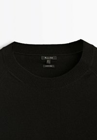 Black knit sweater with a ribbed crew neckline and soft texture. Tag inside shows size information. No visible patterns or hardware.