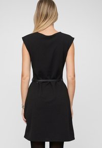 Schwarzes Kleid mit kurzen Ärmeln, tailliertem Schnitt und Gürtel. Glatter, texturierter Stoff mit knielangem Saum und leichter Faltenlegung am Rücken.