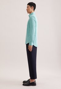 Hellblaues Langarmhemd mit knöpfbarem Manschetten, kombiniert mit dunkelblauen Hosen und schwarzen Slippern, präsentiert ein schlankes Design.