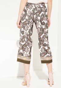 Pantalons cropped à motifs en rose avec un motif paisley complexe, taille élastique et accents vert olive au niveau de l'ourlet. Des talons élégants complètent le look.