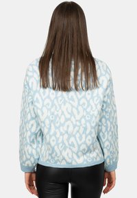 Maglione azzurro chiaro con una texture morbida e pelosa, caratterizzato da un motivo astratto a macchie di leopardo bianche e una vestibilità comoda con polsini a costine.