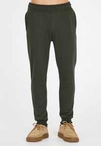 Donkergroene joggerbroeken met een elastische tailleband, zijzakken en taps toelopende pijpen; gecombineerd met tan suède schoenen met rubberen zolen.