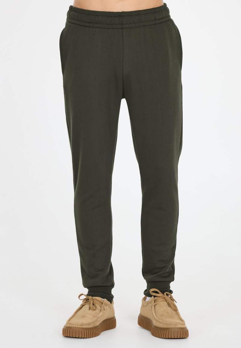 Donkergroene joggerbroeken met een elastische tailleband, zijzakken en taps toelopende pijpen; gecombineerd met tan suède schoenen met rubberen zolen.