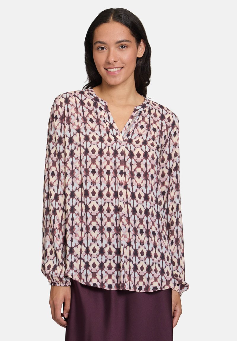 Blusa a maniche lunghe in tessuto leggero con un motivo geometrico viola e crema, dotata di scollatura a V e dettaglio con bottoni al colletto.