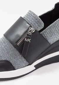 Sneaker slip-on nera e argento metallico con una parte superiore testurizzata, una fascia centrale in pelle e una cerniera laterale con un charm logo.