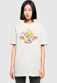 Biely oversized tričko s farebnou grafickou potlačou a textom "Girls Girls Girls", pričom karikatúra je umiestnená pod výstrihom.