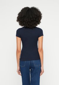 Tmavomodré rebrované tričko s krátkymi rukávmi, okrúhlym výstrihom a priliehavým strihom, doplnené modrými riflovými nohavicami s viditeľným šitím na zadnej strane.