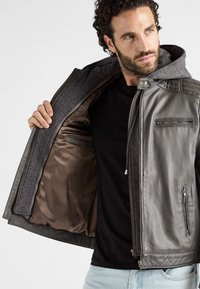 Grijze leren jack met grijze hoodie, ritszakken en een gladde binnenvoering. Gedetailleerde stiksels en metalen hardwareversieringen.