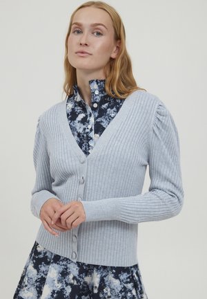 Lichtblauwe geribbelde cardigan met een v-halslijn, knoopsluiting aan de voorkant en licht gepofte mouwen, gecombineerd met een bloempatronen shirt.