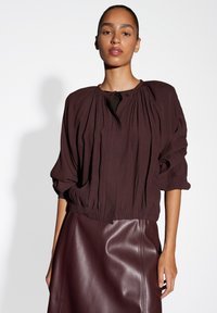 Bordeaux, textuurblouse met geplooid ontwerp, ronde halslijn en gathered manchetten, gecombineerd met een gladde, bijpassende leren rok.