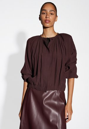 Bordeaux, textuurblouse met geplooid ontwerp, ronde halslijn en gathered manchetten, gecombineerd met een gladde, bijpassende leren rok.