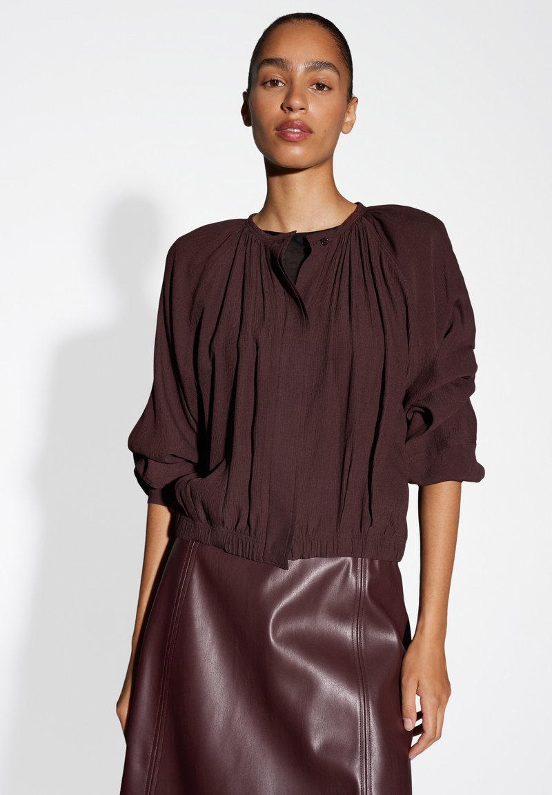 Bordeaux, textuurblouse met geplooid ontwerp, ronde halslijn en gathered manchetten, gecombineerd met een gladde, bijpassende leren rok.