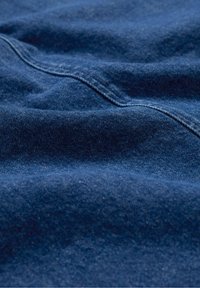 Denimová látka v tmavě námořnické modři s hladkou texturou a jemným vyblednutím. Viditelné švy a jemné záhyby zdůrazňují její splývavost a design.